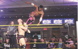 Michael Oku drop kicks Stu Grayson from the top rope.