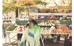 Diane Rochon in costume in front of her stand (Rochon Garden), helping customers with fresh fruit and vegetables